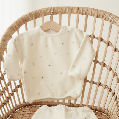 Conjunto de roupa de bebé bege claro com padrões de estrelas numa cadeira de vime