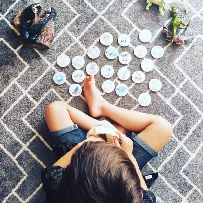 Criança a brincar com fichas e dinossauros num tapete cinzento com padrões brancos