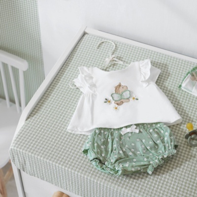 Conjunto de roupa de bebé com camisa branca e calções verdes com bolinhas em tecido xadrez.