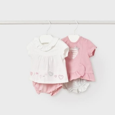 Conjuntos de roupa de bebé, um branco com corações e um rosa com maçã, pendurados em cabides branco sobre fundo branco