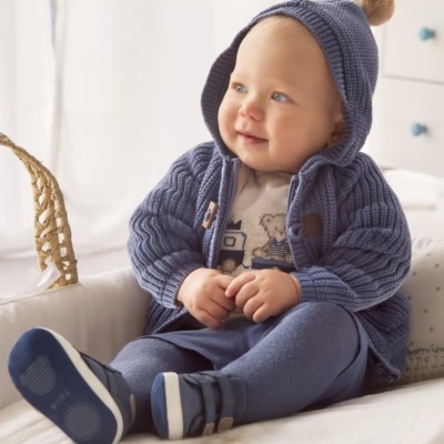 Bebé com camisola de malha azul e capuz com pompom sentado