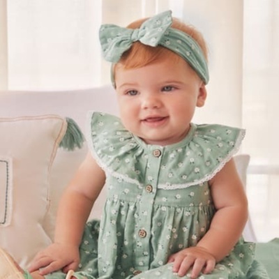 Bebé com vestido verde água com flores brancas e faixa de cabeça a condizer sentada num sofá claro