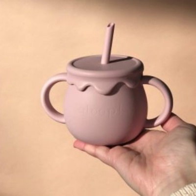 Copo infantil rosa com tampa, canudo e duas pegas segurado por mão