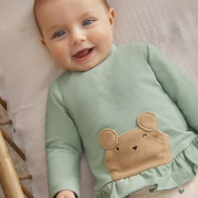 Bebé de camiseta verde claro com bolso com desenho de rato e folho na barra.