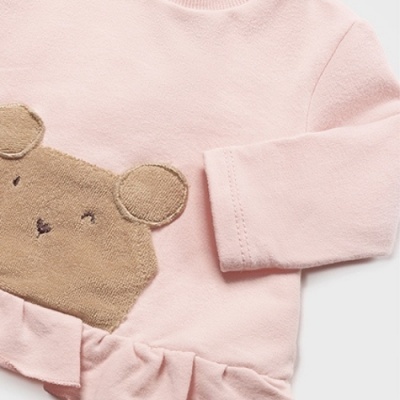Peça de roupa para criança rosa claro com rosto de urso em castanho claro e folho na parte inferior.