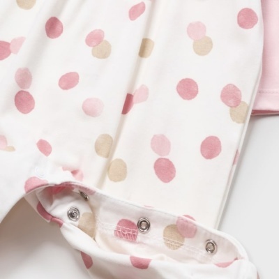 Roupa infantil branca com bolinhas rosa e bege e fechos metálicos na parte inferior