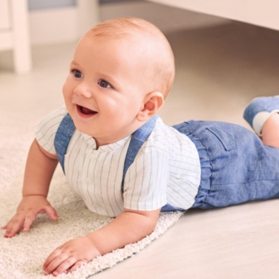 Bebé sorridente rastejando em ambiente interior com roupa azul e branca