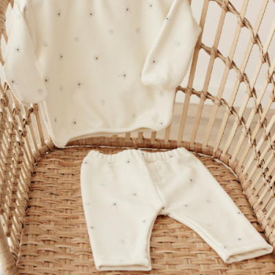 Conjunto de roupa para bebé creme com padrões florais numa cadeira de verga.