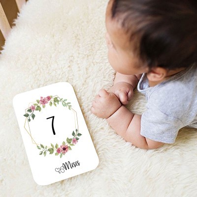 Cartão branco com número 7 e flores e bebé vestido cinzento deitado sobre tapete creme