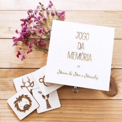 Caixa branca e cartas de jogo da memória em madeira com ilustrações de animais junto a flores roxas secas