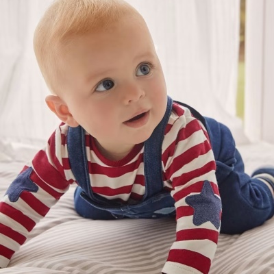 Bebé deitado em cama a usar roupa às riscas e estrelas com calças de ganga.