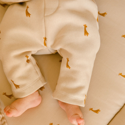 Calças de bebé bege com padrão de girafas castanhas e pés descalços