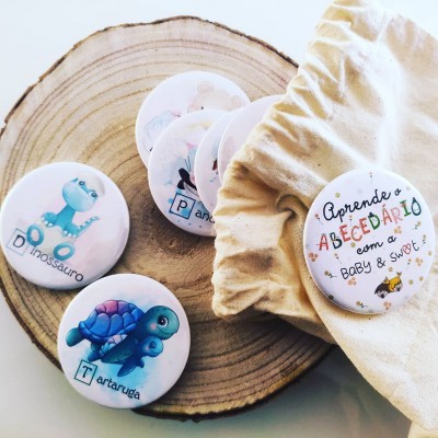Botões redondos infantis com ilustrações de dinossauro e tartaruga sobre madeira e saco de pano com botão maior com texto