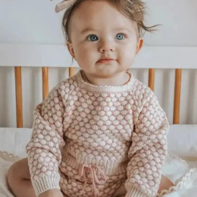 Bebé com fato de malha rosa sentada num berço branco