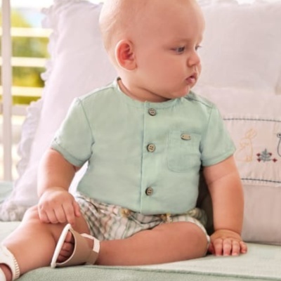 Bebé sentado com roupa verde clara e calças curtas quadriculadas