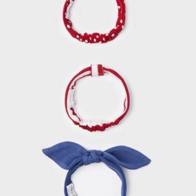 Três fitas de cabelo, uma vermelha com pompons, outra vermelha com branco, e uma azul em forma de laço.