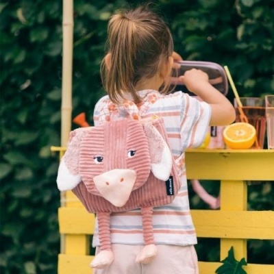 Mochila infantil rosa em forma de elefante com criança de costas junto a mesa amarela