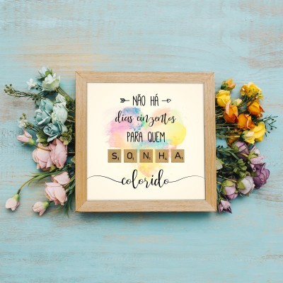 Quadro com texto motivacional em moldura de madeira ladeado por flores coloridas sobre fundo de madeira azul