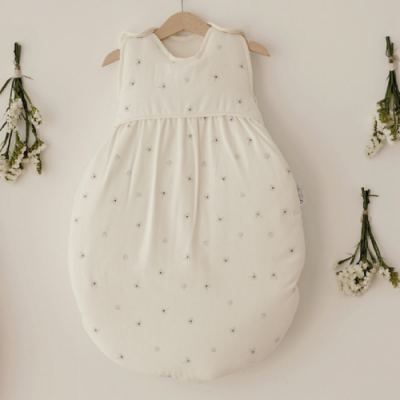 Saco de dormir branco para bebé com pequenas flores cinzentas pendurado na parede