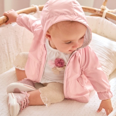 Bebé sentado num berço de madeira com casaco rosa com capuz e roupa clara
