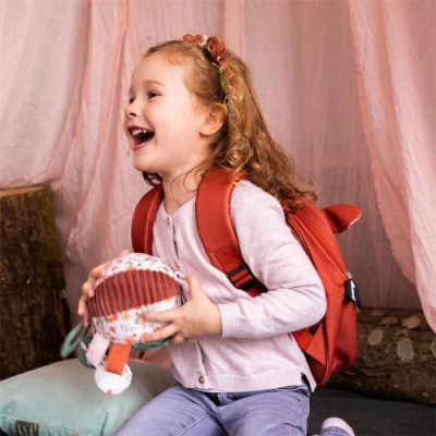 Criança sorridente com mochila vermelha segurando brinquedo de pelúcia colorido