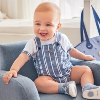 Bebé sentado numa poltrona azul a sorrir, vestido com macacão e sapatos azuis.