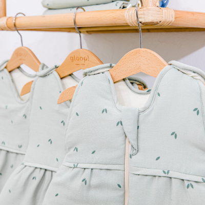 Roupas de bebé verde-claras com padrões de folhas em cabides de madeira