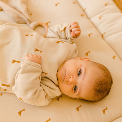 Bebé deitado em colchão bege com padrão de girafas castanhas