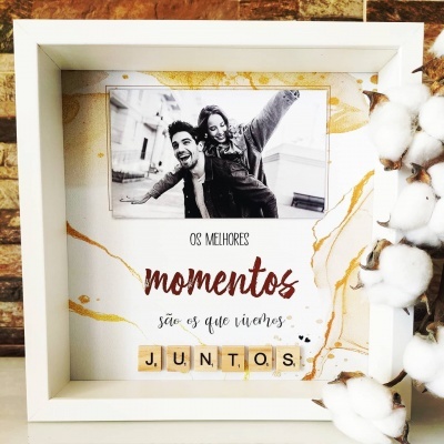 Moldura branca quadrada com foto e texto decorativo em tons bege e dourado, com algodão ao lado