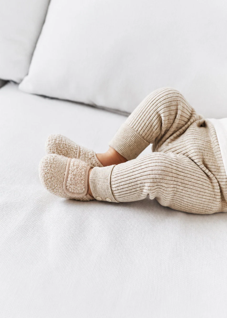 Pés de bebé com pantufas felpudas bege e calças de malha canelada bege