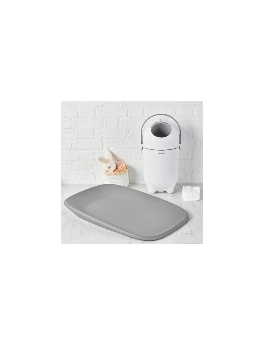 Trocador cinza com balde branco e itens para bebé perto de parede de tijolos branca