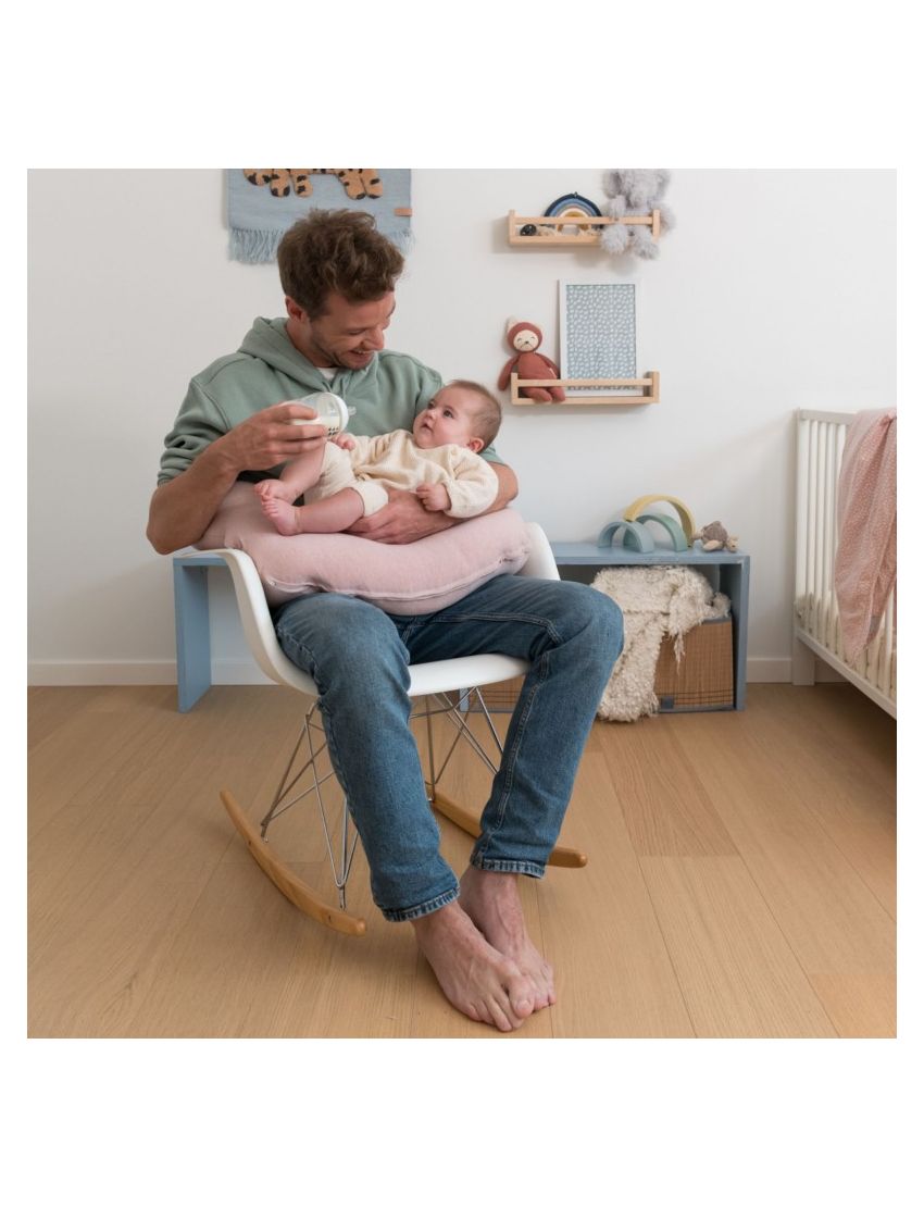 Homem a amamentar bebé numa cadeira de baloiço com almofada rosa numa divisão infantil