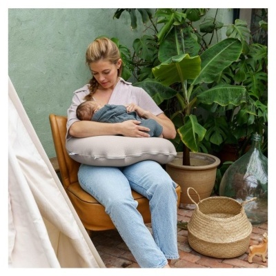 Mulher amamenta bebé com almofada, cadeira castanha, plantas e objetos em pátio