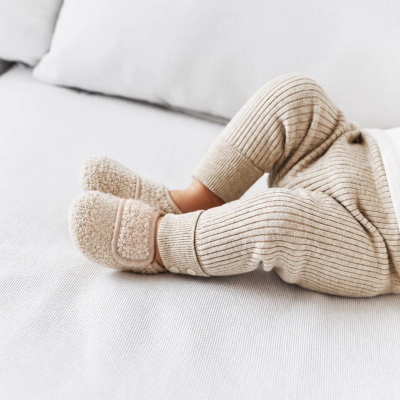 Pés de bebé com pantufas felpudas bege e calças de malha canelada bege