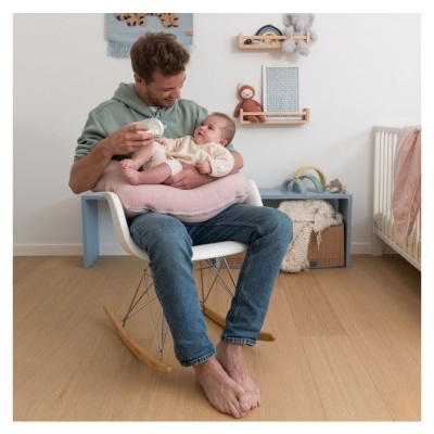 Homem a amamentar bebé numa cadeira de baloiço com almofada rosa numa divisão infantil
