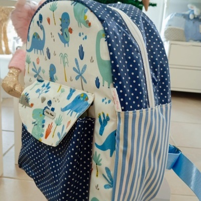 Mochila infantil estampada com dinossauros, com padrões de riscas e pontos, em ambiente interno