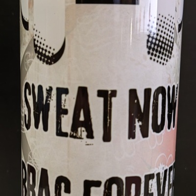 Copo transparente com tampa roxa e texto motivacional impresso.