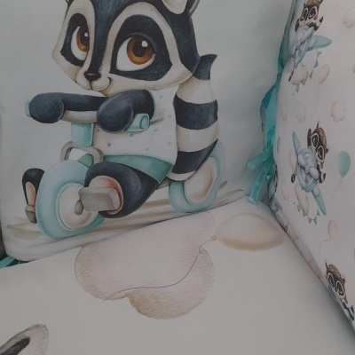 Almofada infantil com estampa de guaxinim a andar de bicicleta em tecido macio, em cama com padrão suave e desenhos de guaxinim.