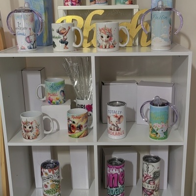 Canecas e garrafas decorativas expostas em estante branca com letras amarelas Baby