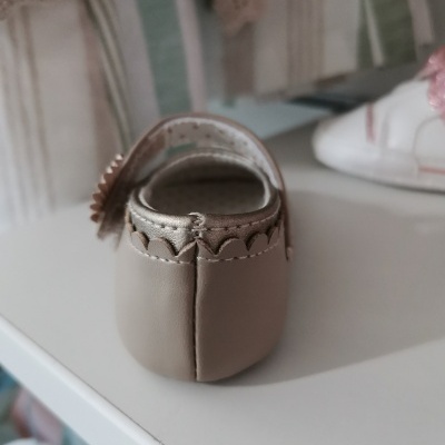 Sapatilha de bebé bege em couro com flores decorativas numa prateleira