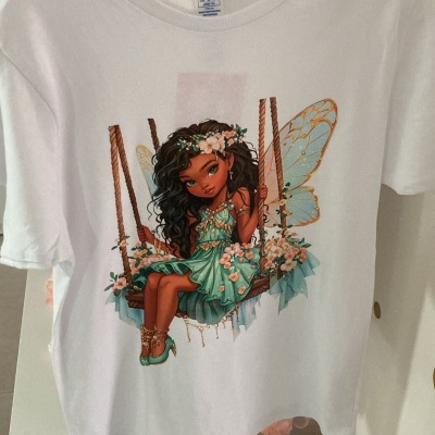 T-shirt branca com estampa de menina fada sentada num baloiço com vestido verde e asas douradas