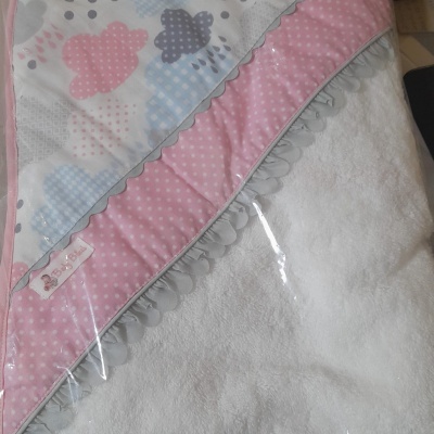 Toalha de bebé branca com capuz com padrão de nuvens coloridas e borda rosa com bolinhas dentro de embalagem