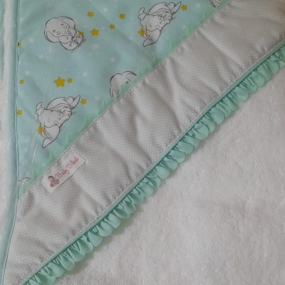 Manta azul claro com estampado de elefantes e estrelas, borda cinza claro com pontos brancos e acabamento ondulado