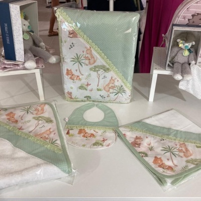 Conjunto de toalhas e babete de bebé com padrão de animais em cores suaves e detalhes em renda, expostos em mesa de loja