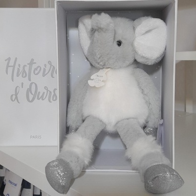 Ursinho de pelúcia cinza e branco numa caixa branca aberta com saco branco ao lado com texto Histoire d'Ours PARIS