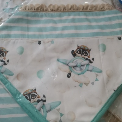 Babete triangular com padrão de guaxinins e aviões em tons azuis e verdes