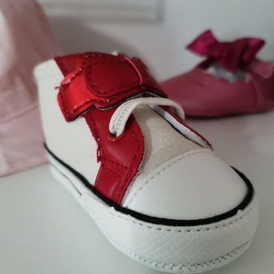 Ténis de bebé branco e vermelho em foco, calçado cor-de-rosa e chapéu rosa ao fundo