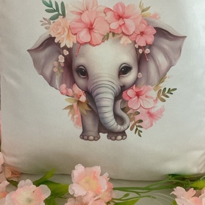 Almofada branca com desenho de elefante bebê e flores cor-de-rosa.