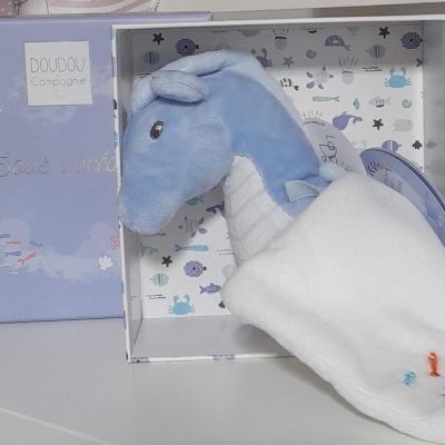 Pelúcia cavalo-marinho azul com tecido branco numa caixa azul desenhada com tema marinho