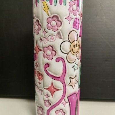 Copo branco decorado com flores cor-de-rosa e brancas, estrelas e uma flor sorridente, com tinta cor-de-rosa a escorrer no topo.